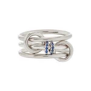 Pode incluir: Um anel de prata com um design único. O anel apresenta várias bandas interligadas com uma pequena seção de pedras preciosas azuis. O anel é uma joia moderna.