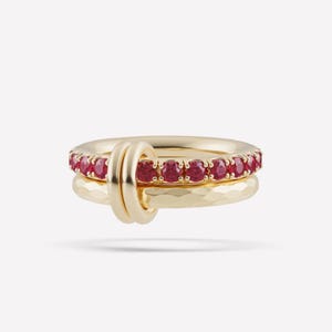 May include: A gold ring featuring two interlocking bands. One band is smooth and set with a row of round, vibrant red gemstones. The second band has a textured, hammered finish. The two bands are joined by a small, smooth gold loop connector.