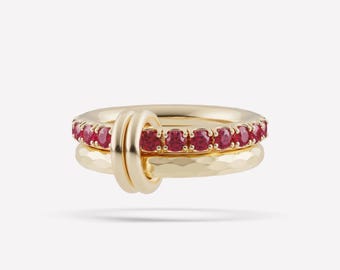Può includere: Un anello in oro composto da due fasce intrecciate. Una fascia è liscia e incastonata con una fila di pietre preziose rosse rotonde e vivaci. La seconda fascia presenta una finitura martellata. Le due fasce sono unite da un piccolo anello d'oro.