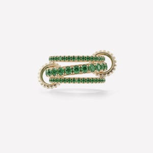 May include: Three gold rings interlocked, each set with a row of bright green gemstones. The rings are connected by gold clasps, with small white gemstones around the edges. The design is elegant and eye-catching.