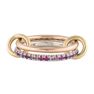 Op de afbeelding: Een ring met meerdere banden, bestaande uit een zilveren band met een rij kleine roze edelstenen, een gladde roségouden band en twee geelgouden cirkelvormige schakels die de banden verbinden. De binnenkant van de zilveren band is gestempeld met 925.