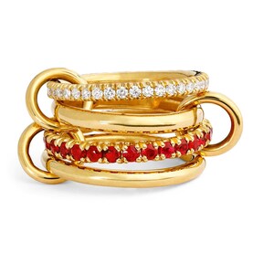 Könnte beinhalten: Ein Stapel aus vier goldfarbenen Ringen, die miteinander verbunden sind. Ein Ring ist mit kleinen, klaren Steinen besetzt, ein anderer mit kleinen, roten Steinen. Die Ringe sind durch große, abgerundete Schlaufen verbunden.