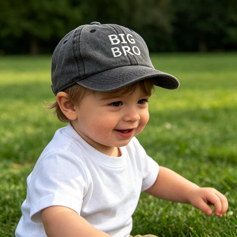 May include: A charcoal gray baseball cap with a distressed, washed-out finish. The front panel features the text BIG BRO embroidered in bold, white, sans-serif capital letters. The cap has a curved brim and a structured crown design.