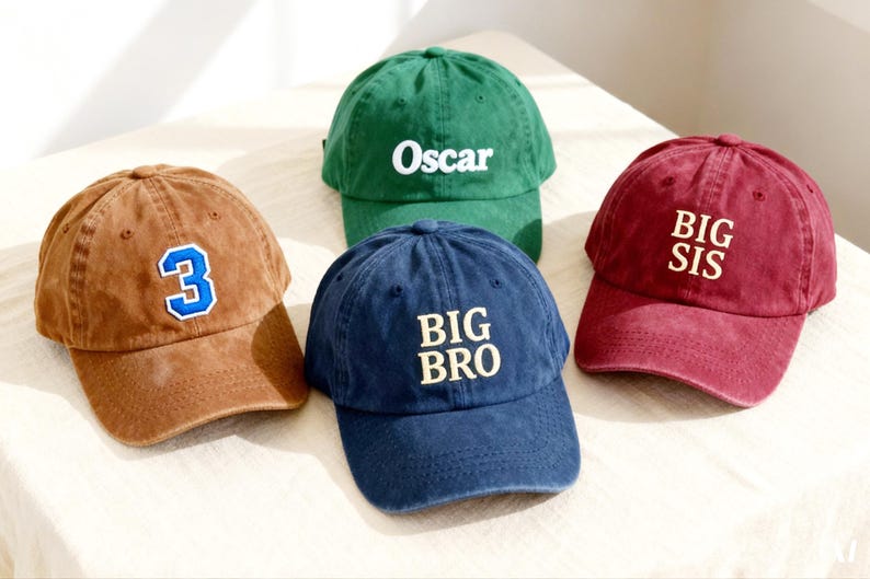 May include: Four baseball caps in brown, green, navy blue, and maroon. The brown cap features a blue and white number 3 patch. The green cap has the white text Oscar. The navy blue cap has the text BIG BRO, and the maroon cap has BIG SIS.