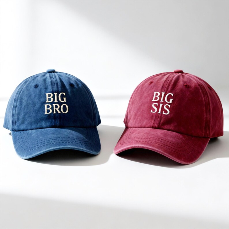 May include: A blue baseball cap with the white embroidered text BIG BRO and a maroon baseball cap with the white embroidered text BIG SIS. Both caps feature a six-panel construction, a curved brim, and a washed fabric finish with visible stitching.
