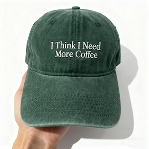 May include: A dark green baseball cap with the white text "I Think I Need More Coffee". The cap features a curved peak and an adjustable strap. The hat is made of a soft, worn material.