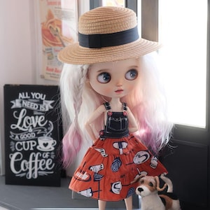 May include: A doll wearing a straw hat with a black band, a denim overall top, and a red patterned dress. The doll is standing next to a small dog figurine. A sign reads "All You Need Is Love, A Good Cup of Coffee."