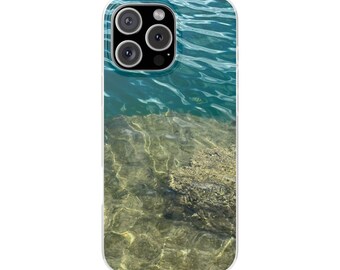 May include: A clear phone case featuring a serene water scene. The top half displays rippling turquoise water, while the bottom half shows a sandy, sunlit seabed. The case has a clear border and a camera cutout.