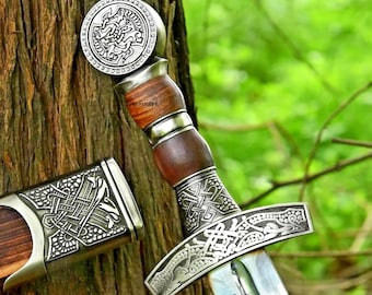 May include: A detailed image of a sword with a wooden handle and a silver-colored guard and pommel. The handle is a dark brown color, and the guard and pommel feature intricate Celtic knot designs. The blade is silver and reflects the light.