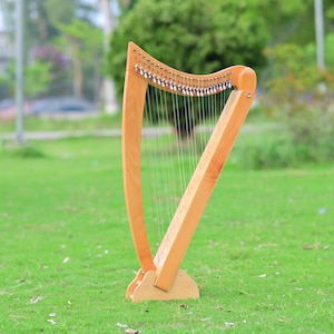 May include: A light brown wooden harp stands on a grassy field. The harp features a curved soundbox and a triangular frame with strings. The harp is a musical instrument, often used in classical music.