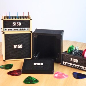 Pode incluir: Modelos de amplificadores de guitarra em miniatura com o texto "5150". Os amplificadores s&atilde;o pretos e bege, com um design de grelha de altifalante. V&aacute;rias palhetas de guitarra coloridas est&atilde;o espalhadas.