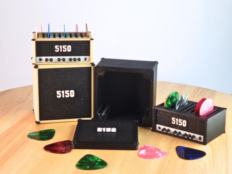 Pode incluir: Modelos de amplificadores de guitarra em miniatura com o texto "5150". Os amplificadores s&atilde;o pretos e bege, com um design de grelha de altifalante. V&aacute;rias palhetas de guitarra coloridas est&atilde;o espalhadas.