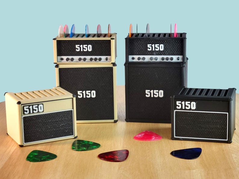 Pode incluir: Cole&ccedil;&atilde;o de organizadores de mesa em miniatura em forma de amplificador, em preto e bege. Cada organizador tem o n&uacute;mero "5150" impresso. Palhetas de guitarra coloridas s&atilde;o exibidas no topo de alguns e espalhadas na superf&iacute;cie.