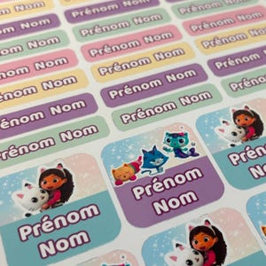 Peut inclure: Feuilles d'étiquettes nominatives colorées avec le texte "Prénom Nom" en différentes couleurs. Certaines étiquettes présentent des personnages de dessins animés. Les étiquettes sont rectangulaires avec des coins arrondis.