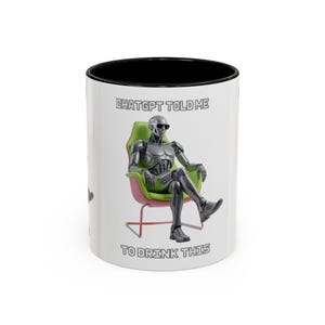 Könnte beinhalten: Weiße Keramik-Tasse mit schwarzem Innenraum. Die Tasse zeigt eine Illustration eines Roboters, der in einem Stuhl sitzt und eine Sonnenbrille trägt. Der Text auf der Tasse lautet "ChatGPT told me to drink this."