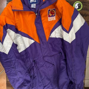 Puede incluir: Chaqueta Starter vintage de los Phoenix Suns en naranja, morado y blanco. Presenta el logotipo de los Phoenix Suns y el logotipo de Starter. La chaqueta tiene cremallera frontal y cuello alto. Una prenda deportiva clásica.