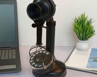 May include: An antique black rotary phone with a large earpiece and dial. The phone has a classic design with a base, a vertical support, and a curved receiver. The dial has numbers and a finger hole. The phone is a vintage decorative item.