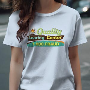 Puede incluir: Una camiseta gris claro con las palabras "Quality Learing Center" en verde y marrón, y el número de teléfono "1-800-FRAUD" en azul y verde. La camiseta la lleva una persona.