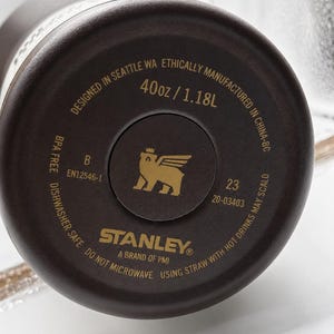 May include: Close-up of the base of a dark brown Stanley water bottle. The base has the brand logo, product details, and the text "40oz / 1.18L". Designed in Seattle, WA, and manufactured in China.