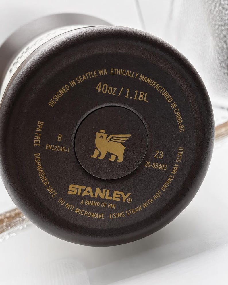 May include: Close-up of the base of a dark brown Stanley water bottle. The base has the brand logo, product details, and the text "40oz / 1.18L". Designed in Seattle, WA, and manufactured in China.