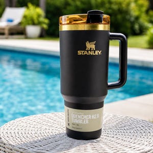 May include: Black Stanley Quencher H2.0 Tumbler with a gold lid and handle. The tumbler features the Stanley logo and the text "QUENCHER H2.0 TUMBLER". Designed for all-day hydration, it holds 1.18L.