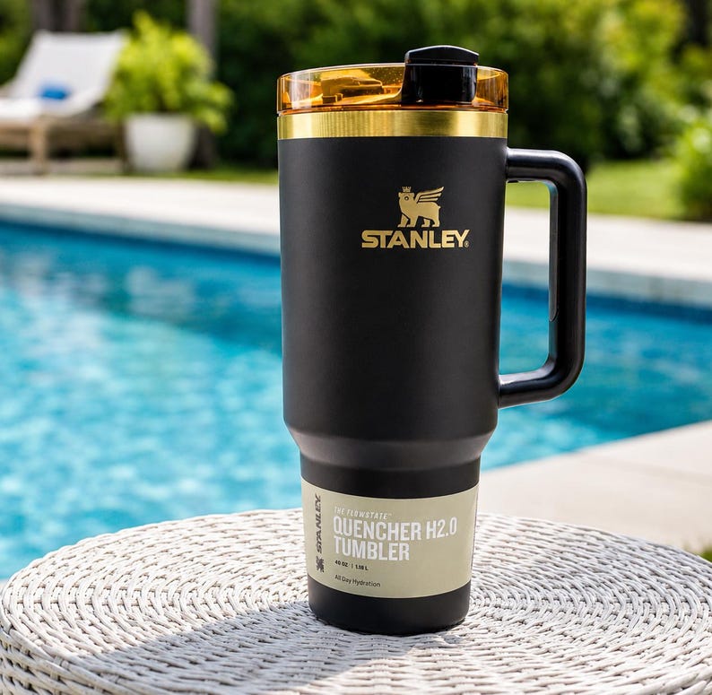 May include: Black Stanley Quencher H2.0 Tumbler with a gold lid and handle. The tumbler features the Stanley logo and the text "QUENCHER H2.0 TUMBLER". Designed for all-day hydration, it holds 1.18L.
