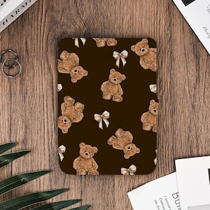 Puede incluir: Un posavasos rectangular marrón con un patrón repetido de osos de peluche y lazos blancos. Los osos de peluche son de color marrón claro con detalles en marrón oscuro. Los lazos son blancos. El posavasos probablemente está hecho de un material duradero.