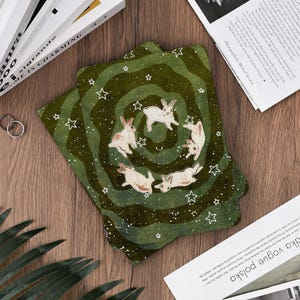 May include: Set of four green coasters with a whimsical design. Each coaster features a spiral pattern with white stars and illustrations of rabbits. The coasters are made of a durable material and are perfect for protecting surfaces from drink rings.