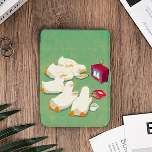 Puede incluir: Funda verde para tableta con una ilustración de patos blancos viendo la televisión. Los patos tienen patas y picos naranjas, con aperitivos y bebidas. El televisor rojo añade un toque de color al diseño lúdico.