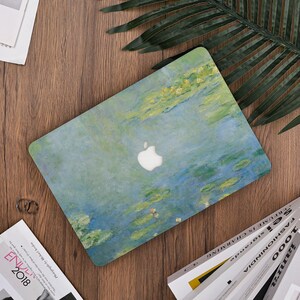 Può includere: Una custodia per laptop con un dipinto di ninfee nei toni del blu, verde e giallo. Il logo Apple è visibile. La custodia è su una superficie di legno, con una foglia verde e delle riviste.