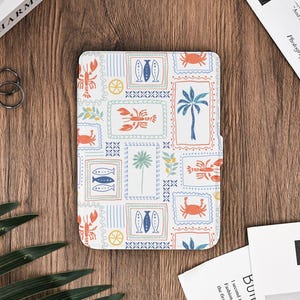 Puede incluir: Una funda blanca para tableta con un diseño estampado colorido con sellos con imágenes de peces, langostas, cangrejos, palmeras y limones. La funda es rectangular y tiene una superficie texturizada.