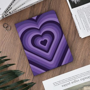 May include: A purple notebook with a heart design. The heart is made up of concentric layers of purple hues, creating a 3D effect. The notebook is rectangular and appears to be closed.