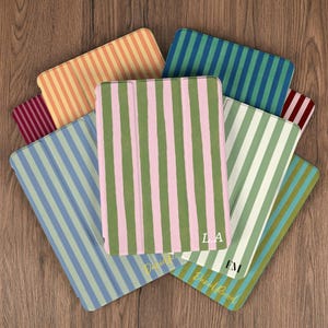 Może przedstawiać: Kolekcja kolorowych etui na tablety z pionowymi paskami w różnych kolorach, w tym różowym i zielonym, niebieskim i zielonym oraz pomarańczowym i żółtym. Niektóre etui mają inicjały i napis "Daniel Russel".