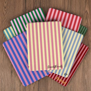 Puede incluir: Una colección de fundas para tabletas con patrones de rayas verticales en varios colores, incluyendo rosa, amarillo, azul, verde y rojo. Las fundas tienen el nombre "Daniel Russell" impreso.