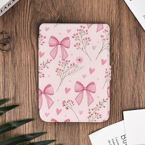 Op de afbeelding: Een roze tablethoes met een herhaald patroon van roze strikken, harten en bloemtakken. De hoes heeft een magnetische sluiting en is ontworpen om de tablet te beschermen. De hoes is gemaakt van een duurzaam materiaal.