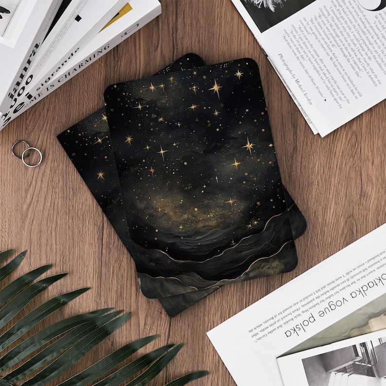 May include: Two rectangular black cards with a celestial design featuring gold stars and a layered, abstract landscape. The cards are stacked on a wooden surface, suggesting a stationery or art print product.