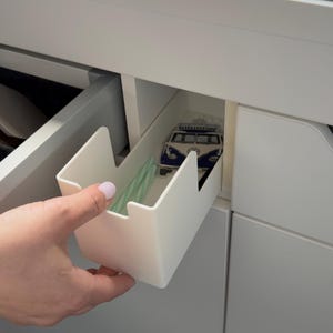 Może przedstawiać: Biały plastikowy organizer szuflady jest wyciągany z białej szafki. W szufladzie znajdują się zielone słomki i niebiesko-biała dekoracja w kształcie VW busa. Szafka ma jasnozielony blat.