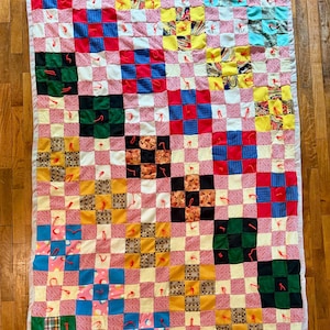 May include: Handmade patchwork quilt featuring a grid pattern of colorful squares. The quilt showcases a variety of fabrics in shades of red, blue, yellow, green, and pink, with a white border. The quilt is approximately 60 inches by 80 inches.
