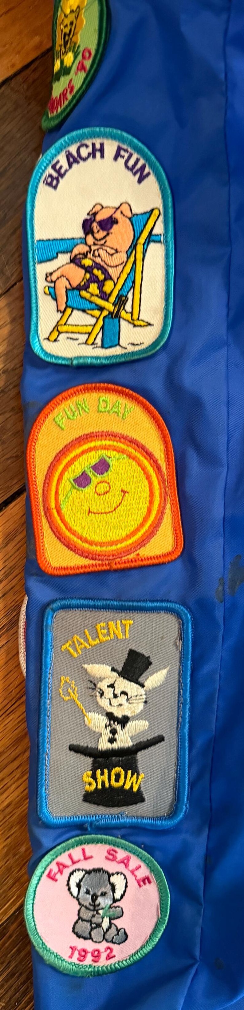 Puede incluir: Una colecci&oacute;n de parches bordados sobre un fondo azul. Los parches presentan varios dise&ntilde;os, incluyendo un oso en la playa, una carita sonriente, un conejo con sombrero de copa y un koala. Los parches tienen texto como "Beach Fun" y "Talent Show".