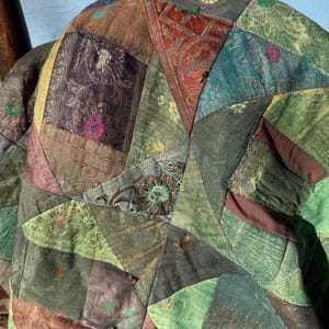 May include: A patchwork textile with a variety of colors and patterns. The fabric is composed of geometric shapes in shades of green, brown, and purple. The design includes floral and paisley motifs, creating a vintage aesthetic.