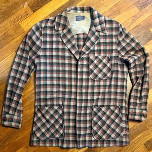 May include: A long-sleeve button-up jacket featuring a plaid pattern in shades of gray, black, and red. The jacket includes a notched collar, one chest pocket, two lower front pockets, and a Pendleton brand label on the inner neck lining.