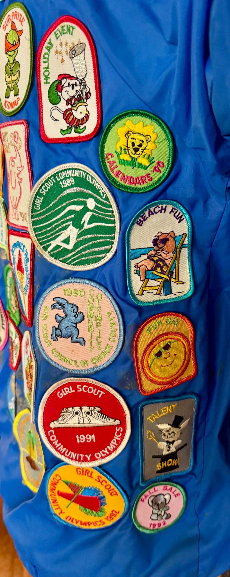 Puede incluir: Una colecci&oacute;n de parches coloridos de Girl Scout sobre un fondo azul. Los parches presentan varios dise&ntilde;os, incluyendo una figura corriendo, un oso en la playa, y textos como "Holiday Event" y "Fun Day".