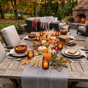 Pode incluir: Uma mesa de jantar de madeira com um caminho de mesa cinza, ab&oacute;boras laranjas e brancas, hastes de trigo, folhas de outono e bolotas. A mesa inclui tigelas de cer&acirc;mica, pratos, talheres, p&atilde;o fatiado e velas em suportes de vidro &acirc;mbar.