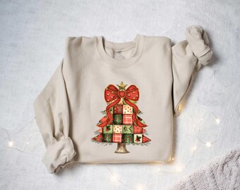May include: Beige sweatshirt featuring a Christmas tree design. The tree is composed of patchwork squares in red, green, and gold, topped with a red bow and gold star. The design is centered on the front of the long-sleeved garment.