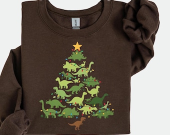May include: A brown sweatshirt featuring a Christmas tree design made of green dinosaurs. The tree is topped with a yellow star and decorated with string lights. The sweatshirt has long sleeves and a crew neck.