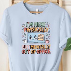 May include: Light blue t-shirt with the text "I'M HERE PHYSICALLY BUT MENTALLY OUT OF OFFICE." The graphic includes a sad laptop, coffee cups, and paperclips. The shirt is a casual wear item.