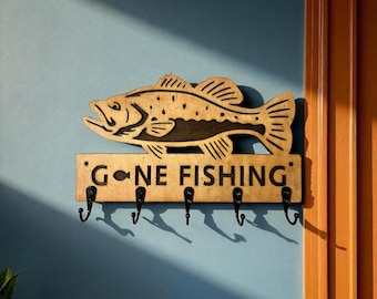 May include: Wooden wall-mounted key holder with a fish design and the text "GONE FISHING." The key holder has five black hooks and is mounted on a blue wall.