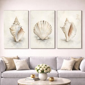 Pode incluir: Um conjunto de três impressões de arte de parede com ilustrações em aguarela de conchas. As impressões da esquerda e da direita exibem conchas em espiral, enquanto a central apresenta uma concha em leque, em tons neutros de bege e branco.
