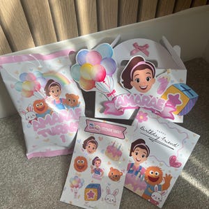 Puede incluir: Un conjunto de art&iacute;culos de fiesta con una ni&ntilde;a de dibujos animados, globos y el texto "AMARAE TURNS 1". Incluye una bolsa de regalo, una caja, una hoja de pegatinas y una tarjeta de cumplea&ntilde;os con el texto "Happy Birthday Friend!"