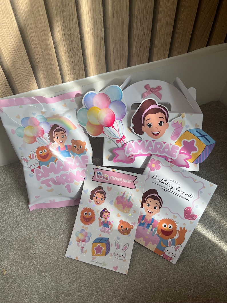 Puede incluir: Un conjunto de art&iacute;culos de fiesta con una ni&ntilde;a de dibujos animados, globos y el texto "AMARAE TURNS 1". Incluye una bolsa de regalo, una caja, una hoja de pegatinas y una tarjeta de cumplea&ntilde;os con el texto "Happy Birthday Friend!"